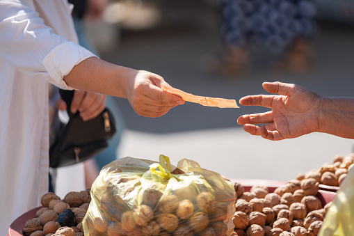 Close up photo of two hands exchanging Turkish paper Lira in farmer's market. Green vegetables are seen on the background. Selective focus on hands. Shot in outdoor with a full frame mirrorless camera.