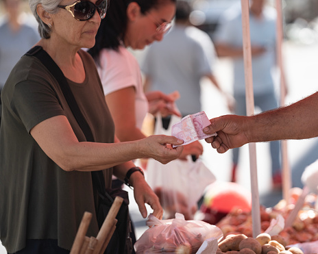 Photo of senior woman and adult friend buying raw food in farmer's market. Shot under daylight.