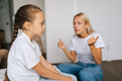 Side view of little girl with blonde mother scolding lecturing difficult kid for bad behavior at home or school. Mad mom arguing shouting at stubborn child daughter.