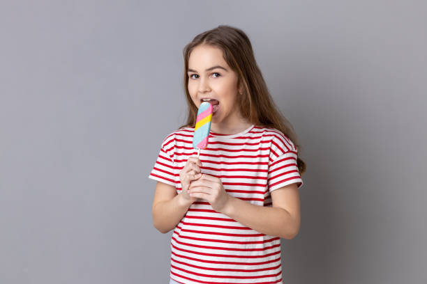 istock Delighted little girl biting colorful candy, looking away with childish satisfied expression. 1480182802
