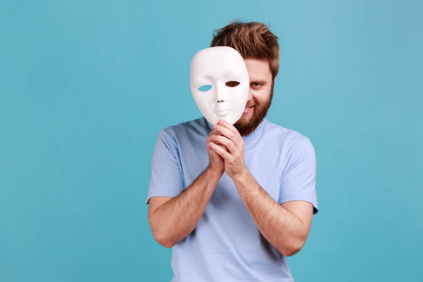 Man in blue T-shirt removing white mask from face showing his smiling expression, good mood. stock photo