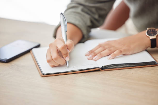 Woman hands, writing and notebook for planning schedule, agenda or list with a pen on an office table. Book, planner or journal with creative ideas, strategy or goals as inspiration for writer person manos de mujer, escritura y cuaderno para planificar horario, agenda o lista con un bolígrafo sobre una mesa de oficina. libro, planificador o diario con ideas creativas, estrategias u objetivos como inspiración para la persona escritora