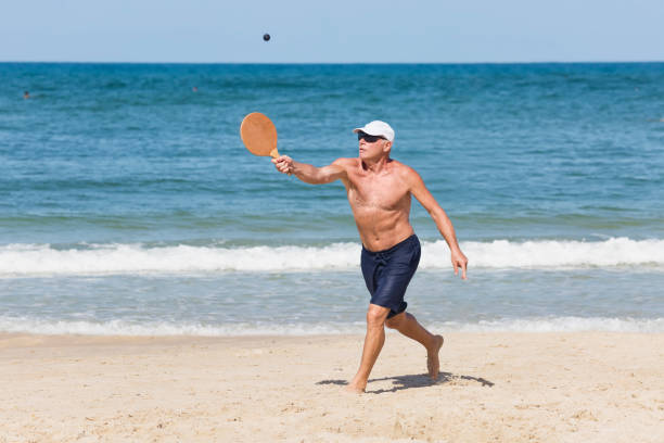 um homem maduro bate uma bola enquanto joga matkot na praia - matkot - fotografias e filmes do acervo