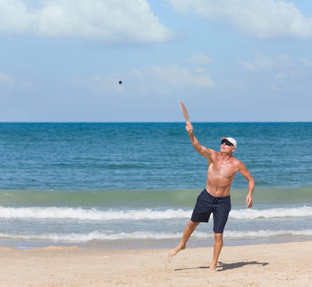 um homem maduro bate uma bola enquanto joga matkot na praia - matkot - fotografias e filmes do acervo