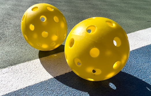 Small Yellow Pickleballs with large background Yellow Pickleball on the boundry line of pickleball court