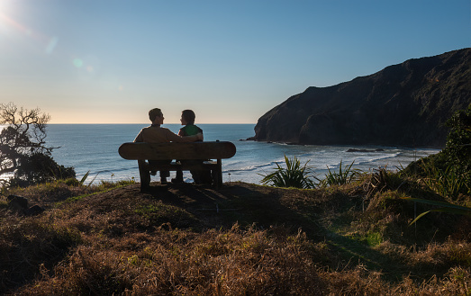 Couple looking at each other, sitting on the bench at Bethells Beach. Couple in love concept. Waitakere. Auckland.