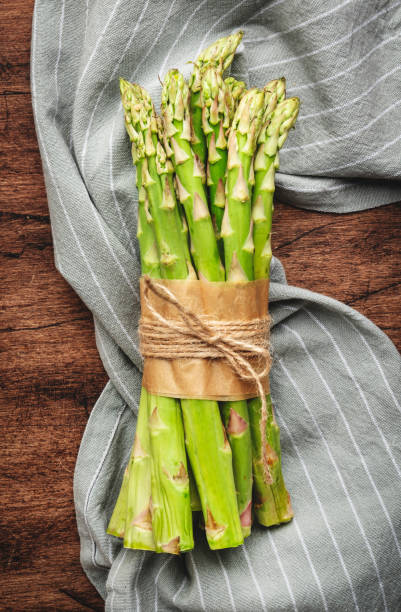 istock Fresh asparagus bunch and gray napkin on rustic wooden kitchen table background, top view, copy space 1480217348