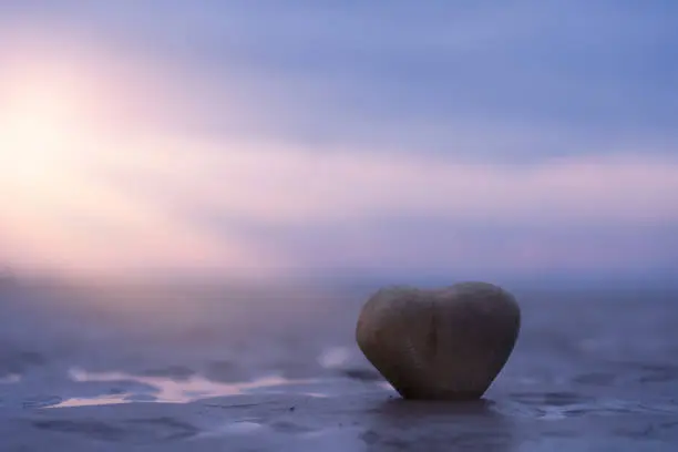 Stone Heart Shape standing on summer beach sand with blurry  purple and blue Sky background,Image Beautiful sea beach with sunset for valentines day, wedding, honeymoon or love greeting card concept