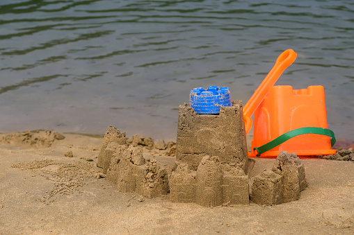 Stock photo showing sandy beach with a sandcastle made with a bucket with a moulded shape and view of lagoon and coastline woodland off island of Goa on a sunny day with clear blue skies.