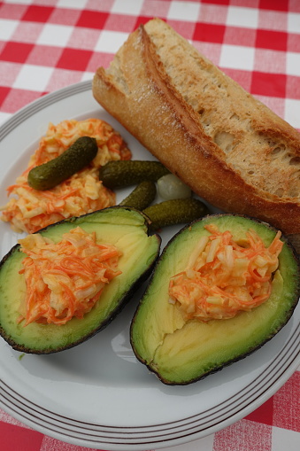 Halved avocado filled with coleslaw served with pickles and french baguette  Meal served