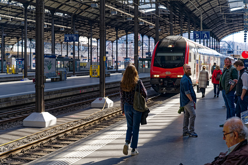 Platform at railway station of Swiss City of Luzern with passengers and train on a sunny spring day. Photo taken March 22nd, 2023, Lucerne, Switzerland.