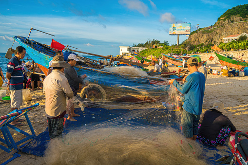 Vung Tau, VIETNAM - AUG 20 2022 : Fisherman casting his net at the sunrise or sunset. Traditional fishermen prepare the fishing net. Fishermen on beach at the Fishing.