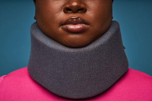 Minimal closeup of unrecognizable black woman wearing neck brace against blue