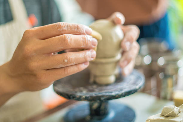 Man potter working on potters wheel making ceramic pot from clay in pottery workshop. art concept. Focus hand young man attaching clay product part to future ceramic product. Pottery workshop.