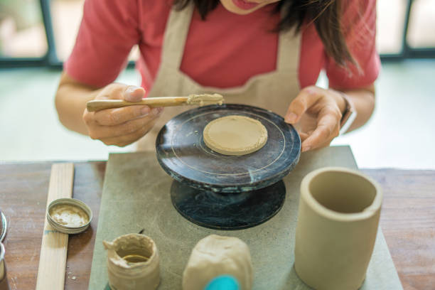 istock Top view Woman potter working on potters wheel making ceramic pot from clay in pottery workshop. Focus hand young woman attaching clay product part to future ceramic product. Pottery workshop. 1480240614