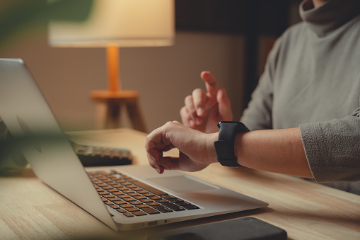 Close-up shot of female's hand checking time or heart rate and pulse on smartwatch sitting at home office.