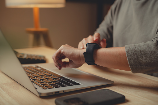 Close-up shot of female's hand checking time or heart rate and pulse on smartwatch sitting at home office.