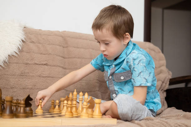 istock Cute little caucasian boy playing chess at home. Young boy intensely develops chess strategy playing board games with friends, sister, brother. Early development and additional education. 1480244143