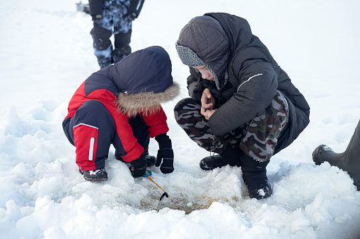 Children in warm clothes holds fishing rod over hole in ice. Ice fishing. Winter sports, family leisure activity and hobby
