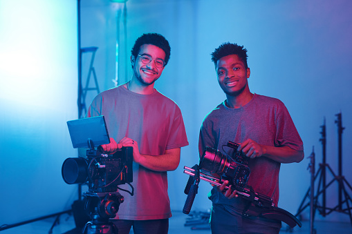 Portrait of young operators smiling at camera while shooting video and photo content in studio