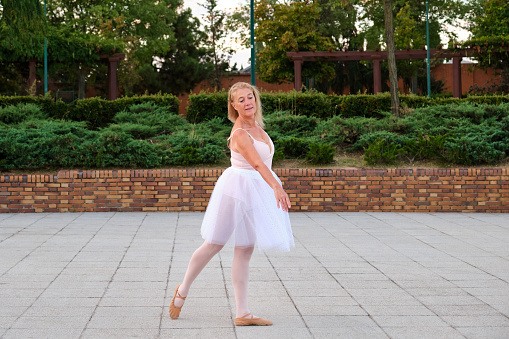 Mature woman dancing ballet in a park at street.