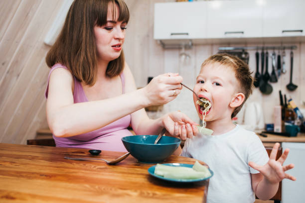 istock Cheerful child eating pasta in the kitchen with mom 1480247756