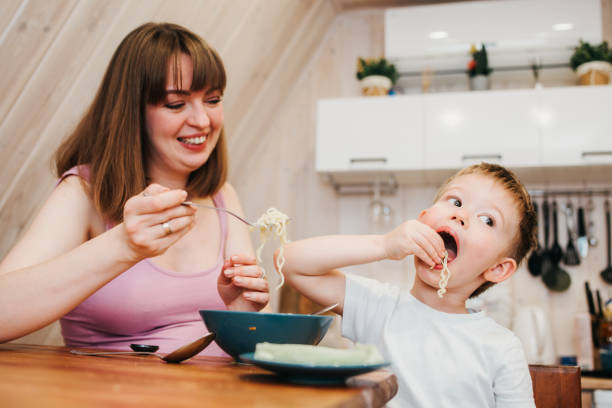 istock Cheerful child eating pasta in the kitchen with mom 1480247855