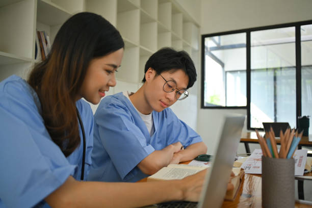 Two male and female medical students talking and using laptop during the lesson in the classroom. stock photo