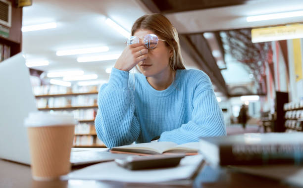 Woman student, fatigue with headache and university burnout, stress for paper deadline or study for exam in library. Campus, college and tired studying with scholarship problem and mental health pain stock photo