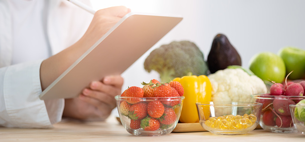 Panoramic of hand professional nutrition healthful surrounded by a variety of fresh fruits and vegetables working on digital tablet. Concept of right nutrition, diet and healthcare.