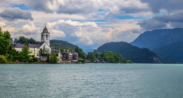 Sankt Wolfgang, Austria, July 10, 2022: View of the catholic St. Wolfgang Church (German: St. Wolfgang Kirche) on the shore of the Wolfgangsee Lake in Upper Austria under cloudy summer sky. The region is also known as Salzkammergut part of wich is listed as UNESCO World Heritage Site.