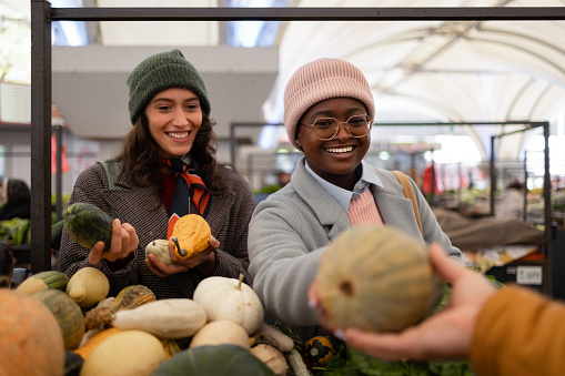 Happy female customers buying organic pumpkins from a salesperson on farmer's market. Focus is on black woman.