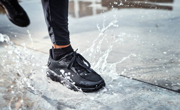 Feet splash water in street, person running in the rain and shoes in puddle of Seattle road for outdoor cardio. Runner training for marathon, step on wet ground and moving fast for fitness exercise los pies salpican agua en la calle, la persona corre bajo la lluvia y los zapatos en el charco de seattle road para cardio al aire libre. entrenamiento del corredor para maratón, pisar suelo mojado y moverse rápido para hacer ejercicio físico