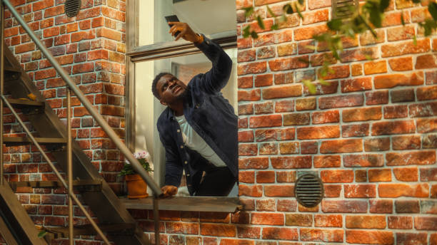 istock Distressed Young Black Man Doesn't Understand Why There is No Cellular Connection on His Smartphone, Frantically Reaching Out to the Sky with a Mobile Phone from His Apartment Window. 1480264003