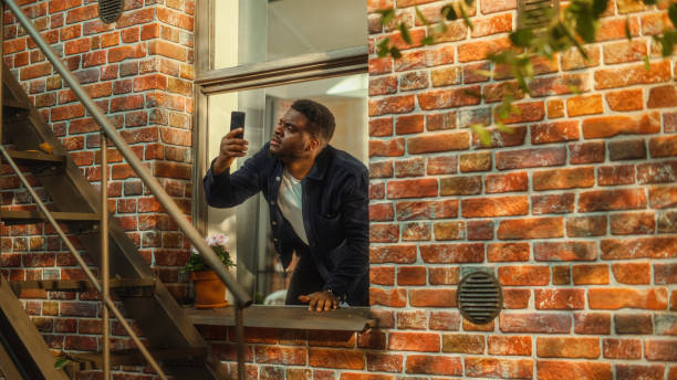 istock Distressed Young Black Man Doesn't Understand Why There is No Cellular Connection on His Smartphone, Frantically Reaching Out to the Sky with a Mobile Phone from His Apartment Window. 1480264025
