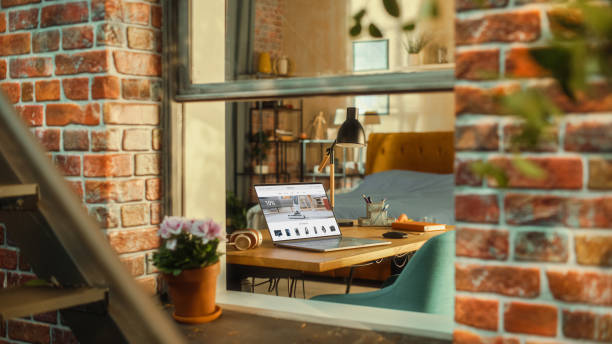 Laptop Computer with Online Shopping Website Display Standing on a Table in Stylish Living Room. View from Outside the Window of a Brooklyn-Style Brownstone Building. Work from Home Concept.
