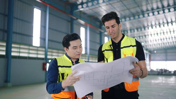 istock Two professional engineer male worker talking and discuss to work holding and looking at paper work in factory Industrial 1480264422