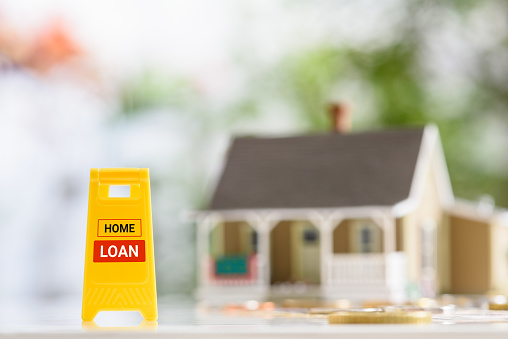 Mortgage loan, home equity loan, housing concept : Yellow warning sign board with the word HOME LOAN, a model house and coins on a table, depicting a loan used by purchasers to raise fund to buy asset