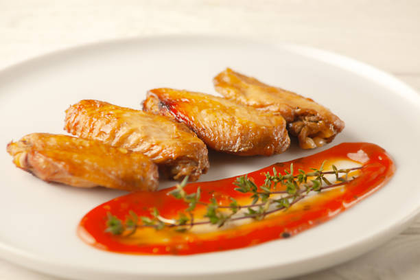Grilled spicy chicken wings with ketchup on a plate on a white background. View from above