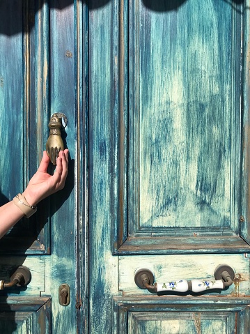 Blue wooden door and a woman's hand holding a brass handle, Kas, Turkey