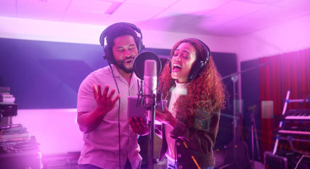 istock Technology, singer or musicians on neon studio microphone or music lyrics app in night recording. Singing people, collaboration or artists on tablet production, voice media or light sound performance 1480274506