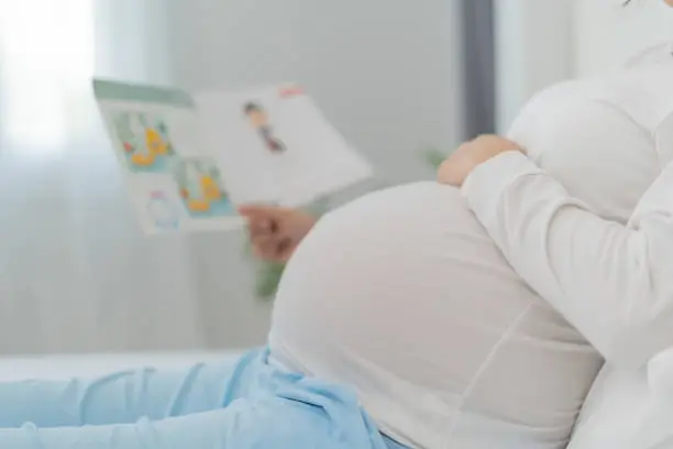 Photo of Pregnant woman is reading a story book to her baby. Reading to your child improves the brain and auditory development of the unborn child. love, family, strengthens, bonds, intelligence.