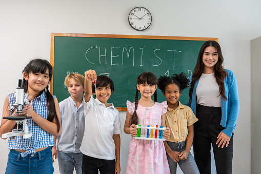 Portrait of diverse children student in classroom at elementary school. Attractive woman instructor teacher standing with young kid after teaching a music subject lesson with happiness at kindergarten