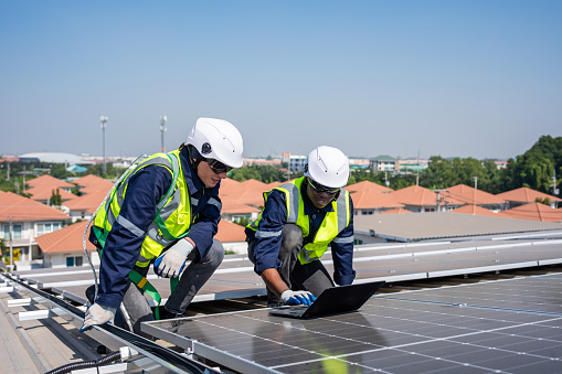 Professional engineer work to maintenance of photovoltaic panel system. Attractive technician worker working on roof inspect and check solar cell panels equipment box at solar cell field during sunset