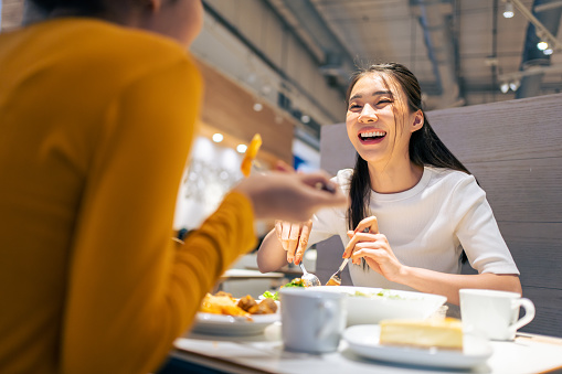 Asian beautiful women having dinner with friend in restaurant together. Attractive young girl feeling happy and relax, having fun talking and eating food at their table in dining room in cafeteria.
