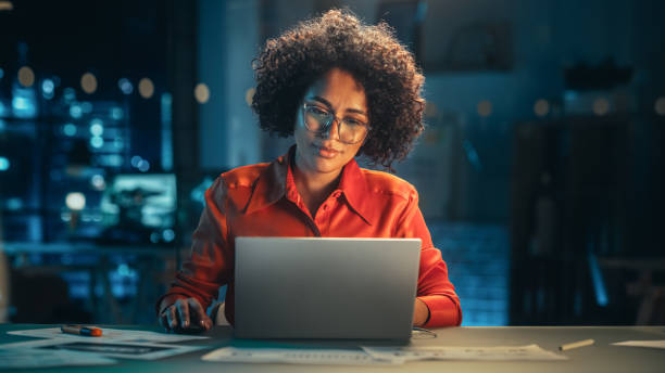 istock Young Black Female Working on Laptop Computer in Creative Office in the Evening. Happy Multiethnic Project Manager Writing Emails, Researching Project Plan Details Online. 1480281346
