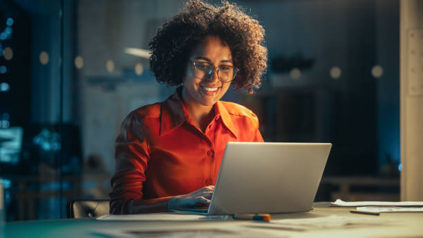 istock Young Black Female Working on Laptop Computer in Creative Office in the Evening. Multiethnic Project Manager Writing Emails, Getting Happy and Surprised When Receiving a Message from a Colleague. 1480281375