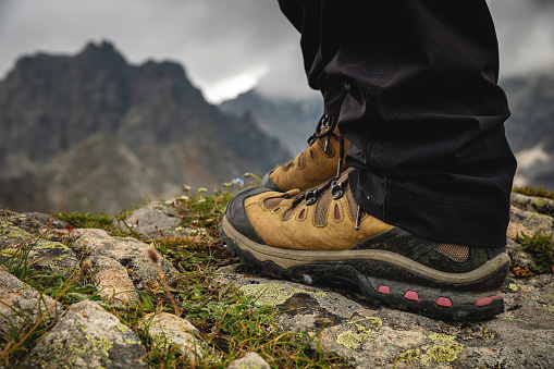 Close-up of legs in trekking boots against the backdrop of an alpine mountain range in a valley.