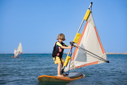 A child who learns to surf in the sea at a beautiful sunset, close-up, windsurfing lessons and school. With copy room.