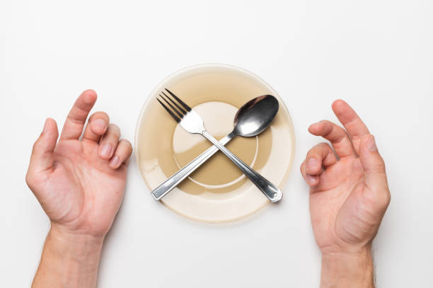 istock Male hands, an empty plate with a fork and a spoon on a white background, top view. Hunger and food delivery concept 1480284138